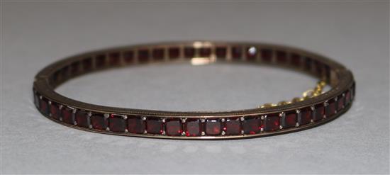 An Edwardian gold and garnet set hinged bangle,